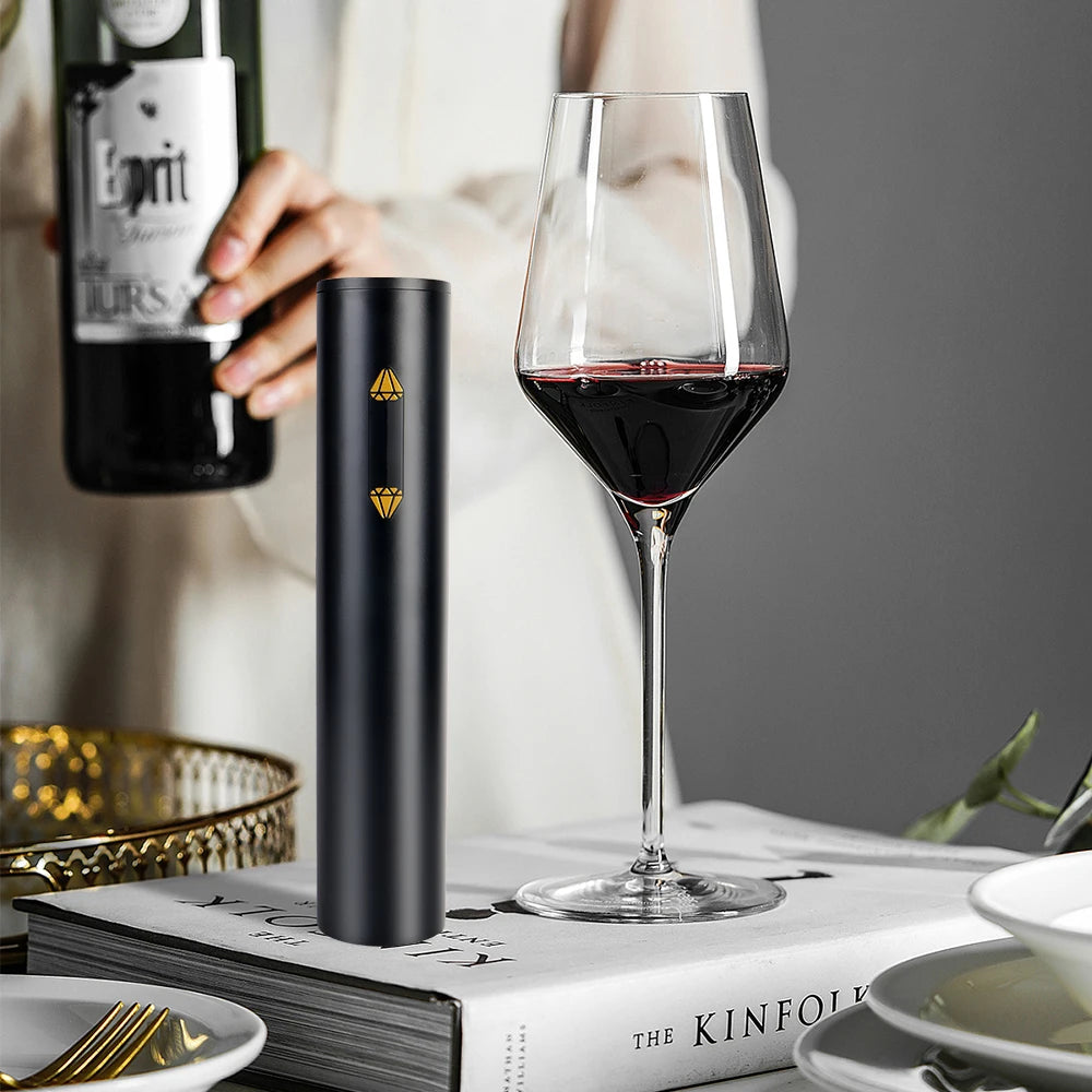 Black electric wine opener next to glass of red wine on a book titled Kinfolk.