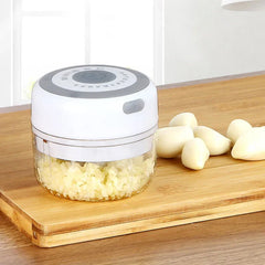 Electric garlic chopper with minced garlic inside, whole cloves beside it.