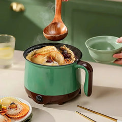 Green electric pot cooking soup with chicken, a wooden ladle and bowl nearby.